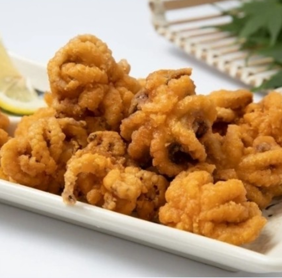 A close-up of golden-fried calamari or baby octopus served on a white rectangular plate with a lemon wedge.