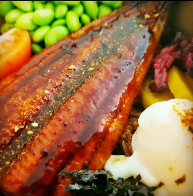 A close-up of a delicious unagi dish with edamame, tomato, and a creamy sauce.