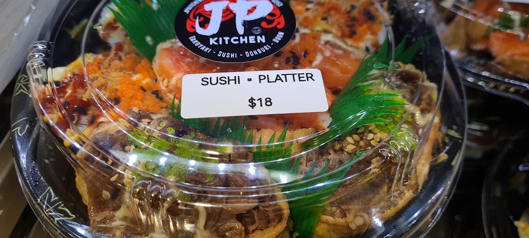 A close-up of a JP Kitchen sushi platter in a clear container with a price tag.