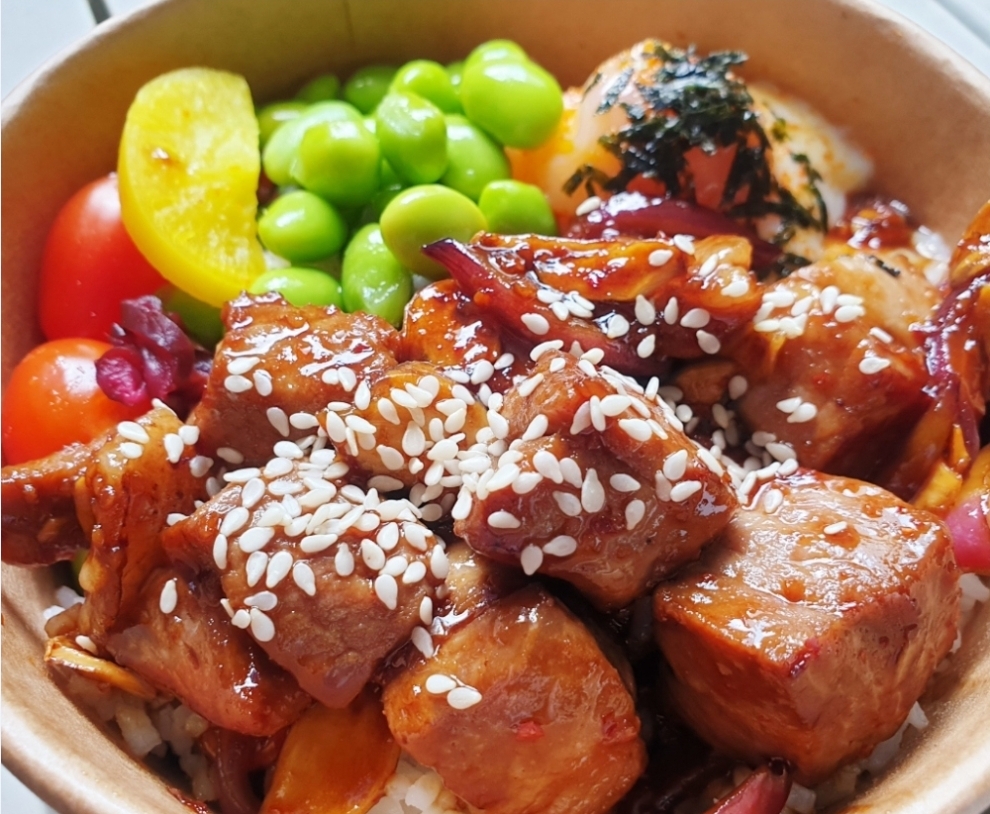 A close-up of a delicious rice bowl featuring glazed chicken, edamame, and a soft-boiled egg.