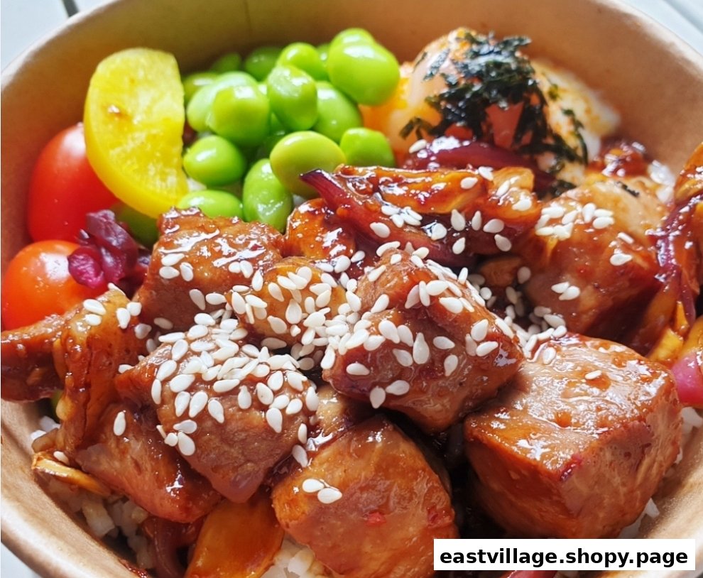 A close-up of a delicious rice bowl featuring glazed chicken, edamame, and a soft-boiled egg.