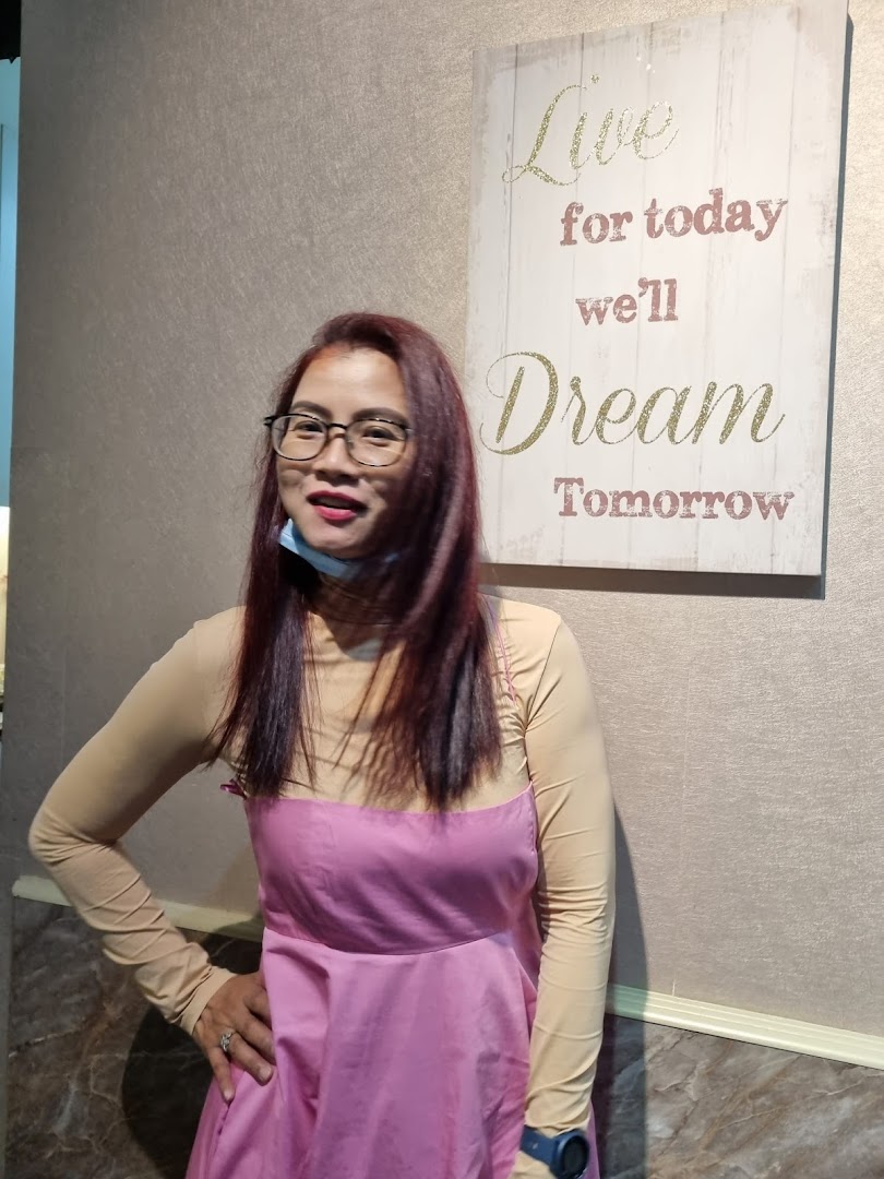 A woman with red hair and glasses stands next to a motivational sign inside the salon.