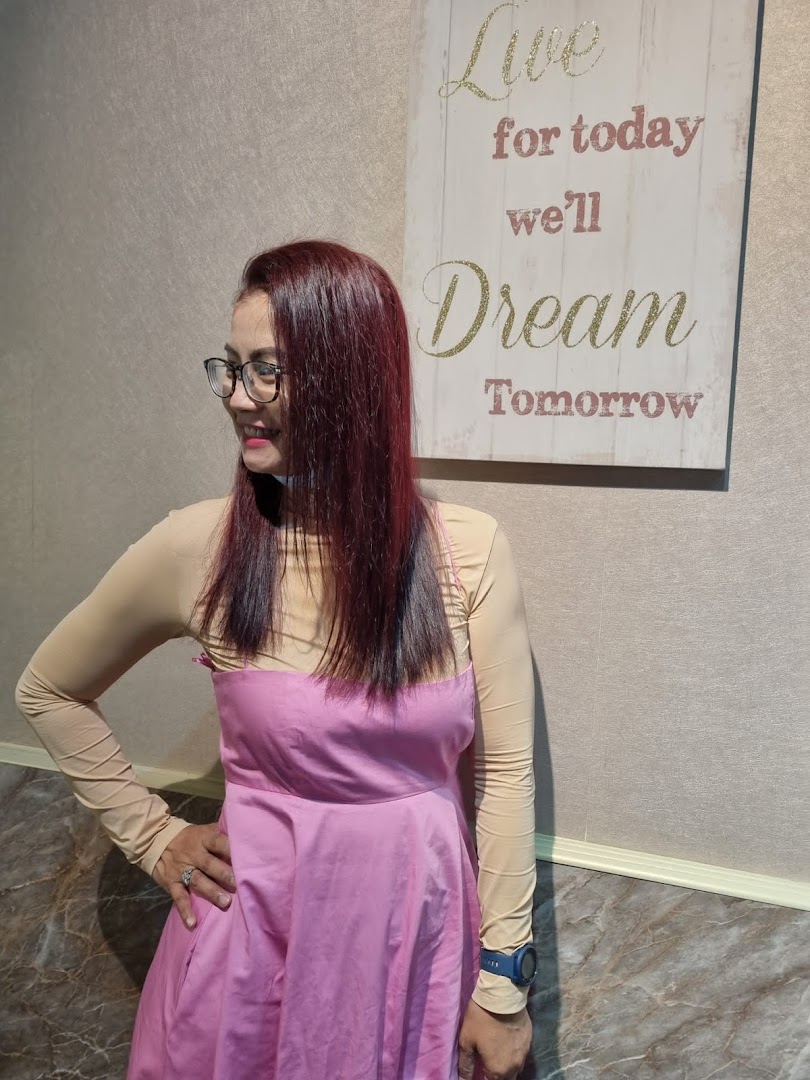 A woman with vibrant red hair smiles, showcasing a stylish look next to a motivational wall decor.