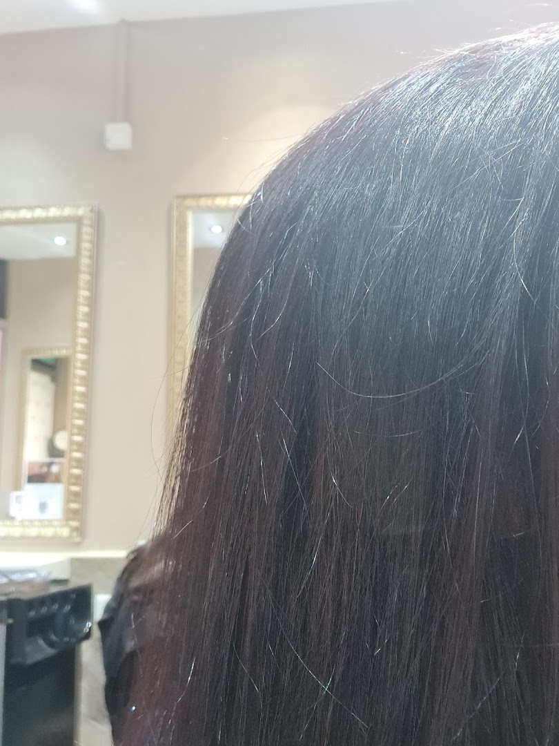 Close-up of a client's dark hair inside a salon, with ornate mirrors in the background.