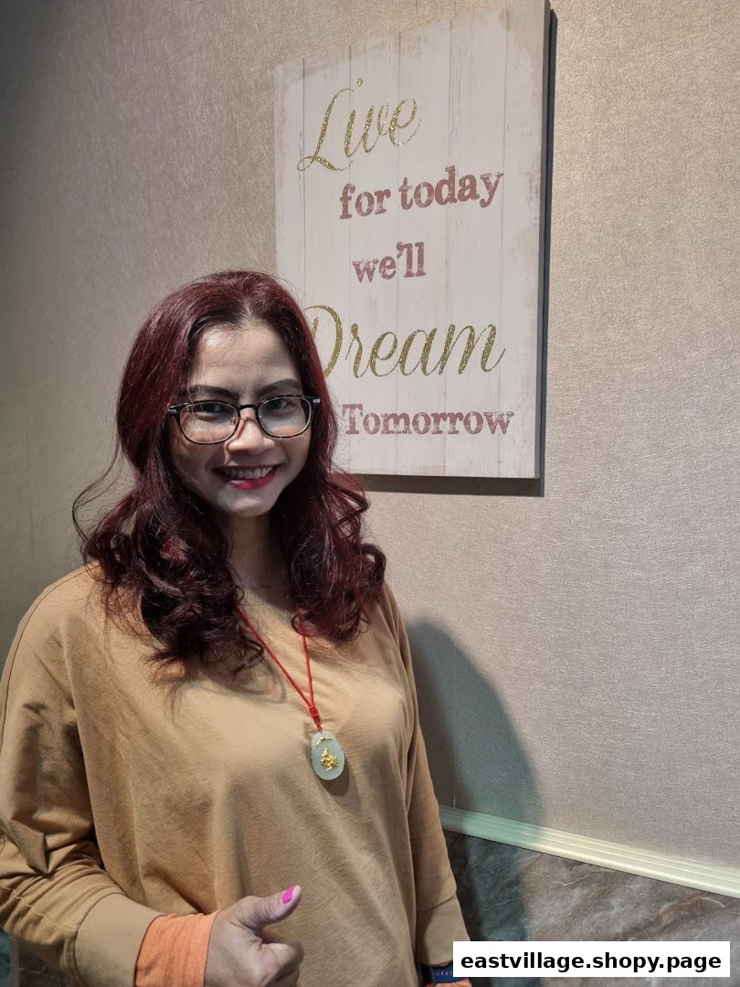 A smiling woman with red hair and glasses stands next to a motivational sign inside the salon.