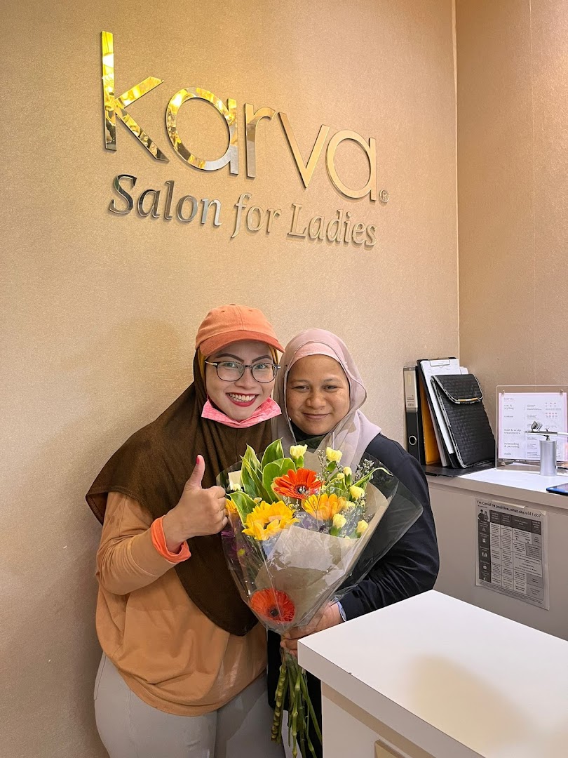 Two smiling women with flowers inside KARVA Salon for Ladies, featuring the shop's logo.
