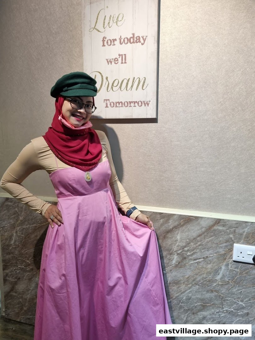 A woman in a pink dress and green hat smiles in a salon interior with a motivational sign.