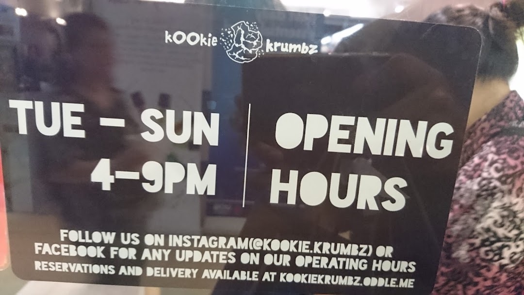 A sign displaying KookieKrumbz's opening hours (Tue-Sun, 4-9 PM) and social media contact information.