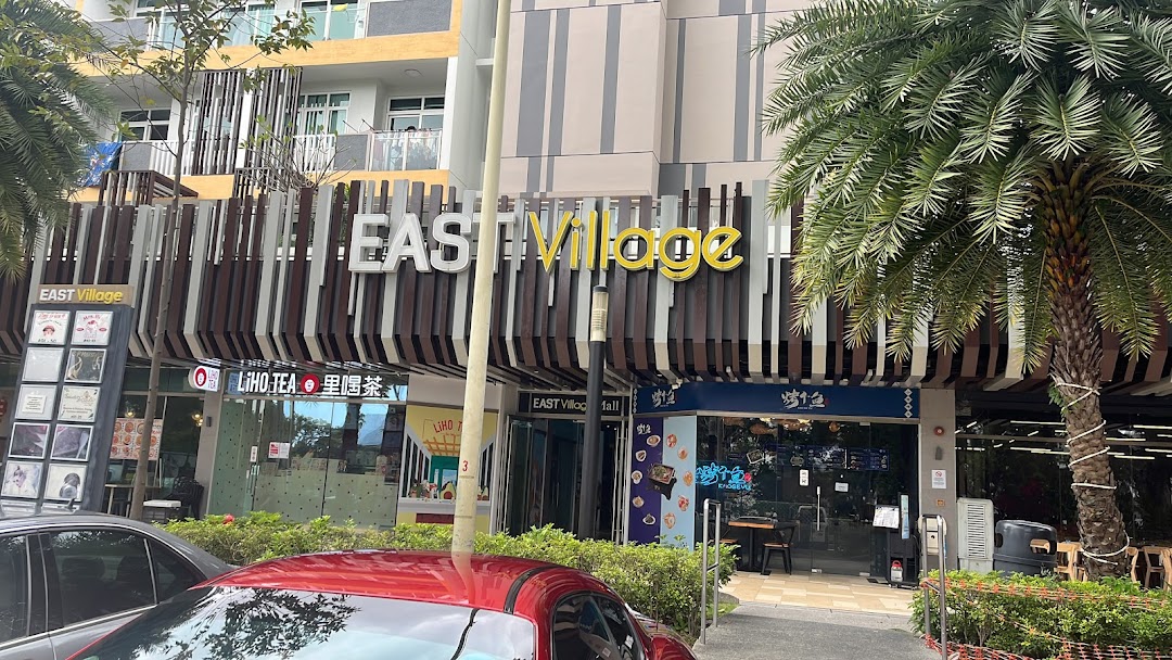 Exterior view of the East Village complex featuring multiple shopfronts and lush palm trees.