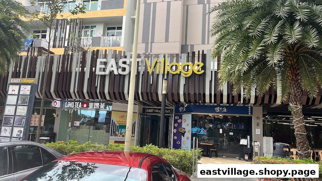 Exterior view of the East Village complex featuring multiple shopfronts and lush palm trees.