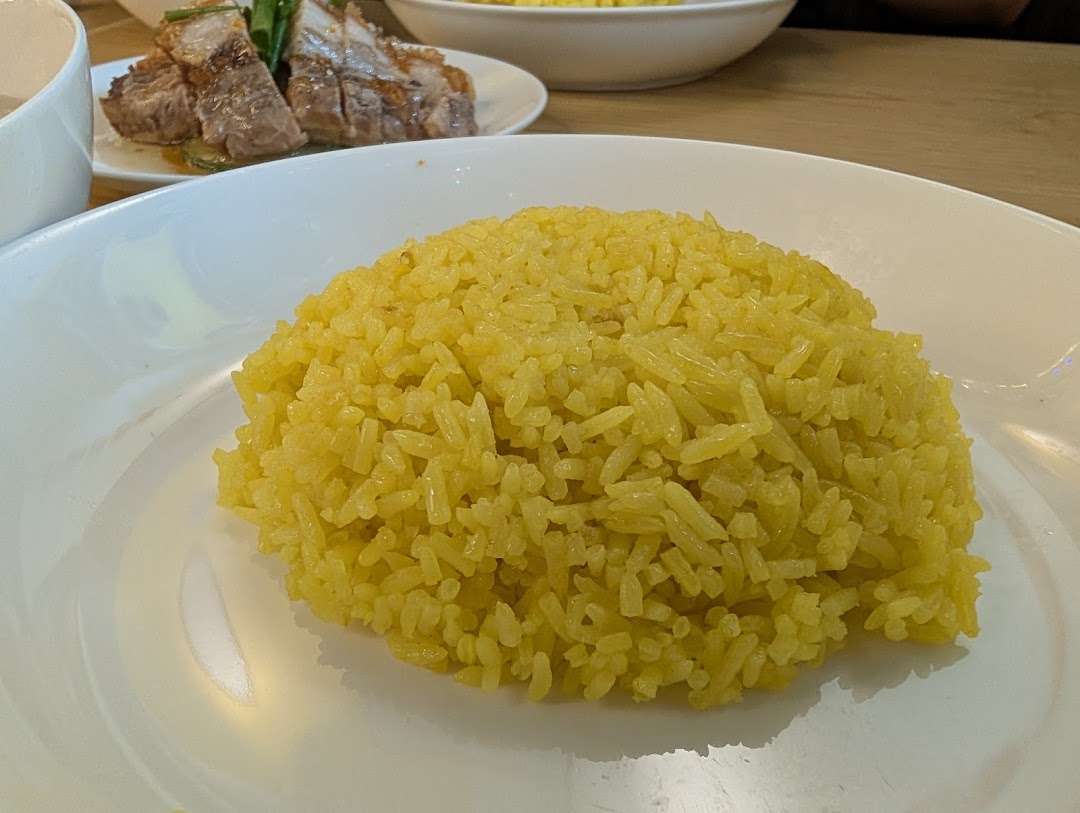 A close-up of fragrant yellow chicken rice served on a white plate.