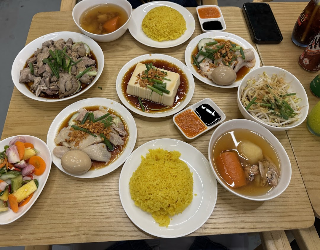 A vibrant spread of chicken rice dishes, sides, and soups on a wooden table.