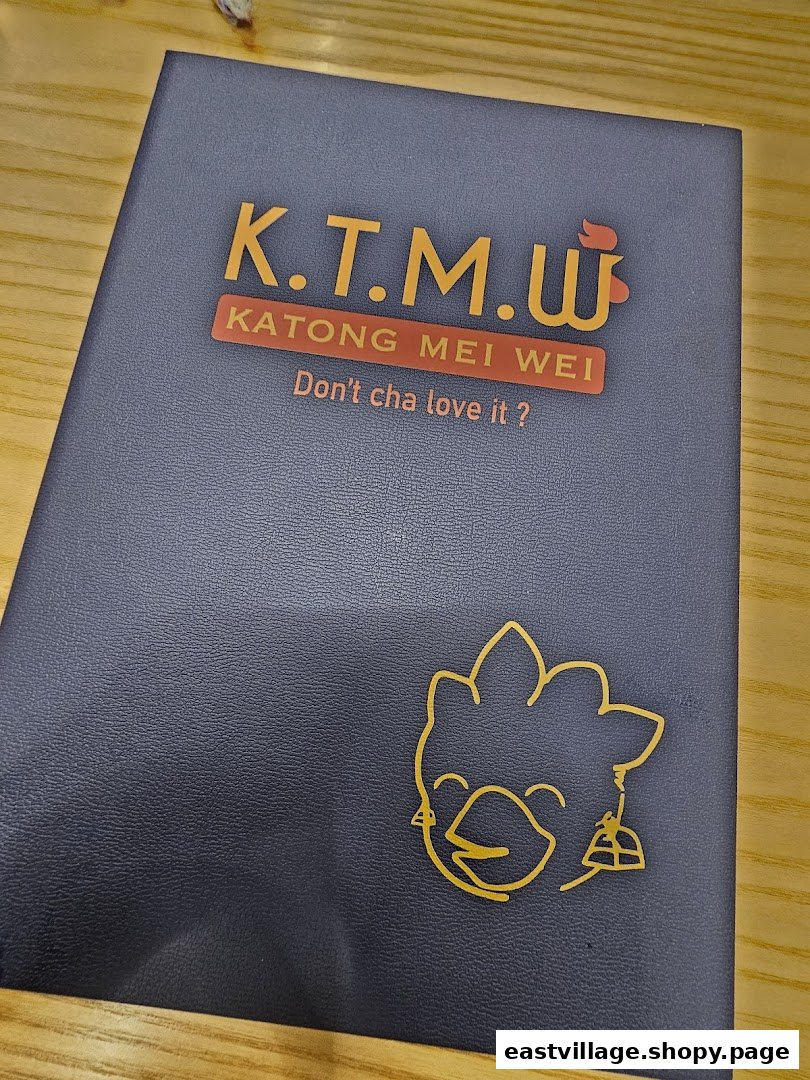 Close-up of a dark blue folder/menu cover featuring the KTMW Katong Mei Wei logo and slogan.