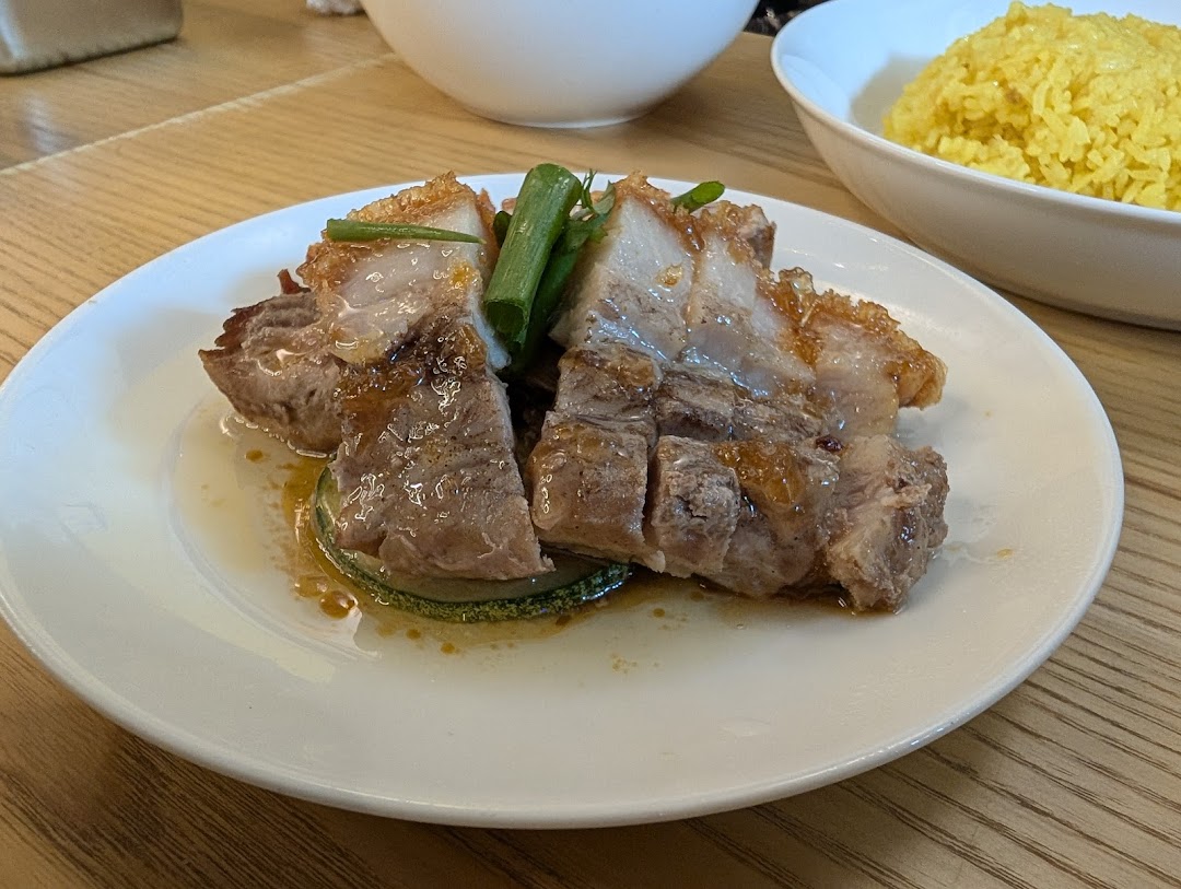 A plate of crispy roasted pork belly with sauce and green onions, served with yellow rice.