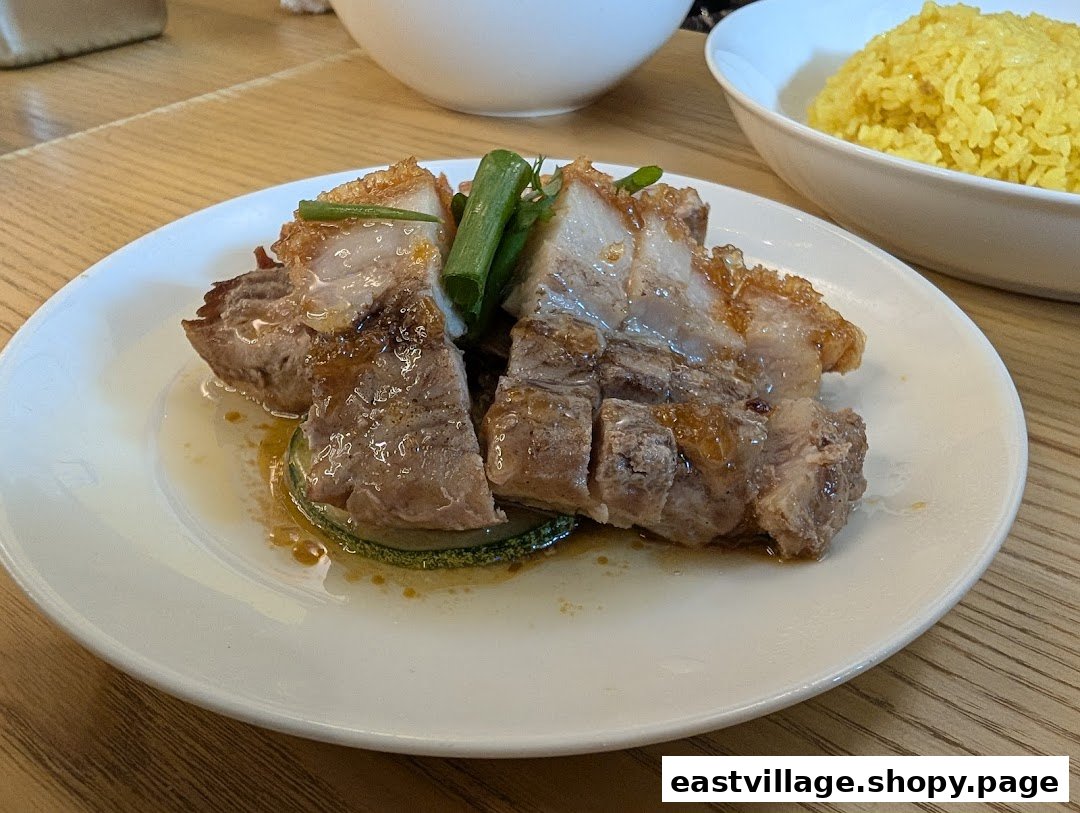 A plate of crispy roasted pork belly with sauce and green onions, served with yellow rice.
