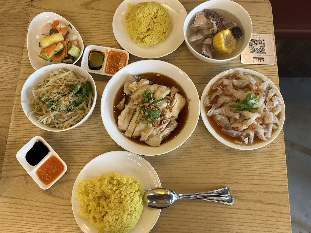 A delicious spread of Hainanese chicken rice, sides, and soup on a wooden table.