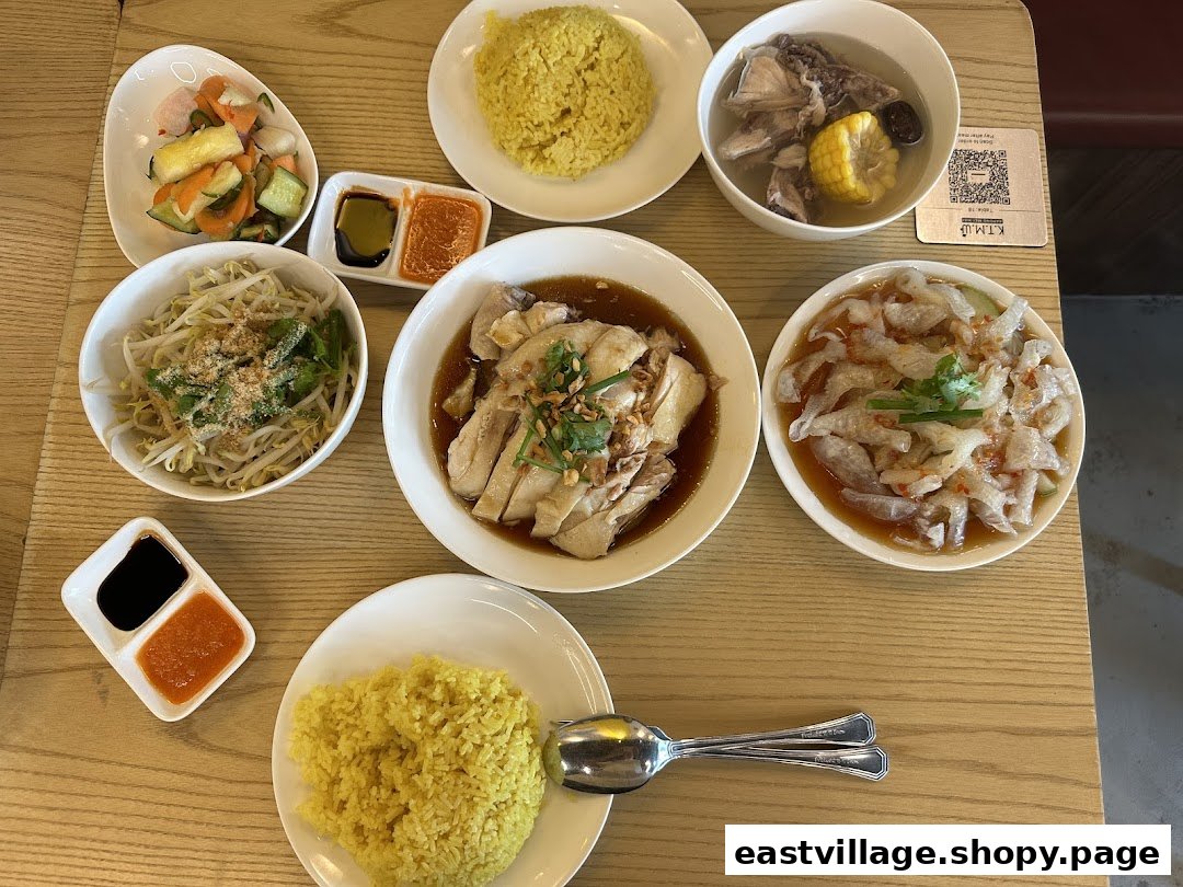 A delicious spread of Hainanese chicken rice, sides, and soup on a wooden table.