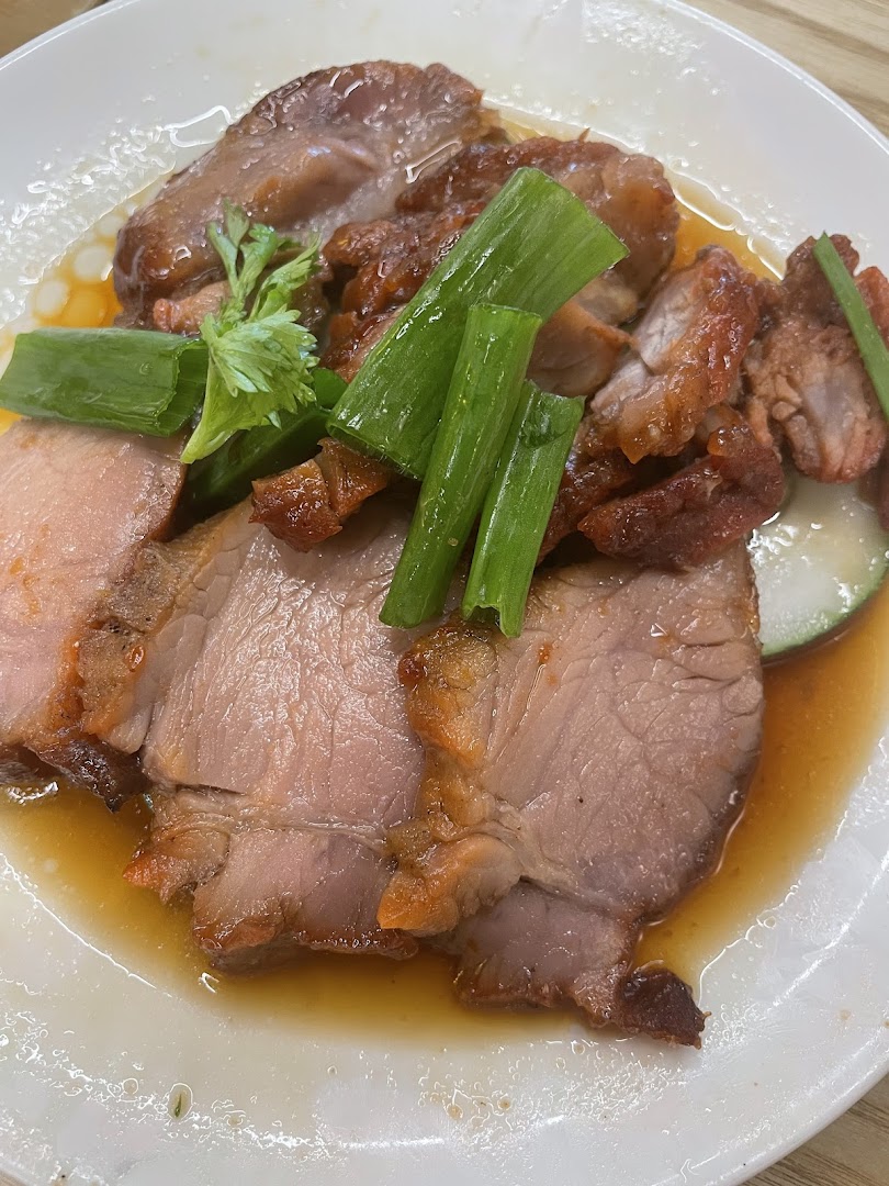 A close-up of succulent roasted pork slices with crispy skin, garnished with spring onions and savory sauce.