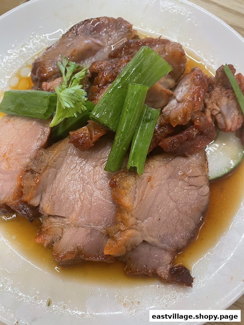 A close-up of succulent roasted pork slices with crispy skin, garnished with spring onions and savory sauce.