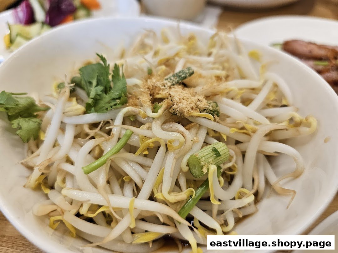 A close-up of blanched bean sprouts topped with herbs and seasoning in a white bowl.