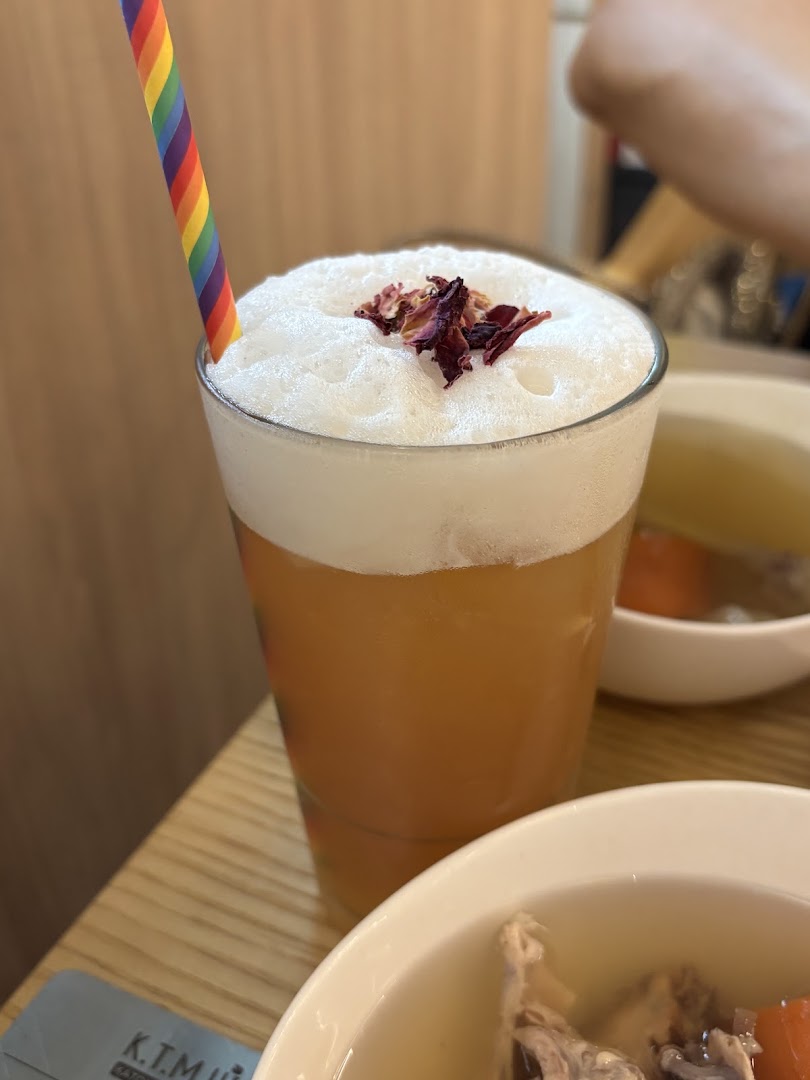 A refreshing foamy drink topped with dried petals and a rainbow straw, served alongside a bowl of soup.