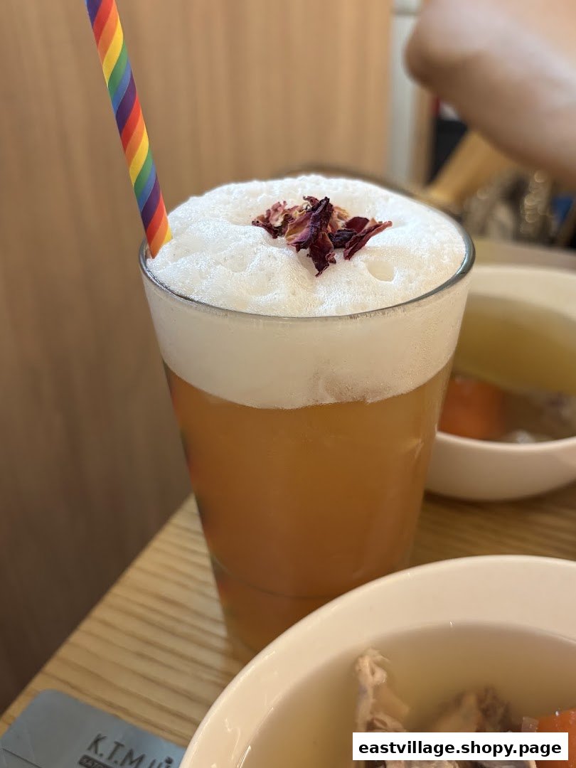 A refreshing foamy drink topped with dried petals and a rainbow straw, served alongside a bowl of soup.