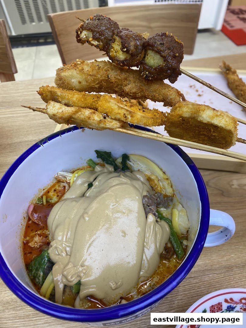 A bowl of spicy malatang with peanut sauce and crispy fried skewers.