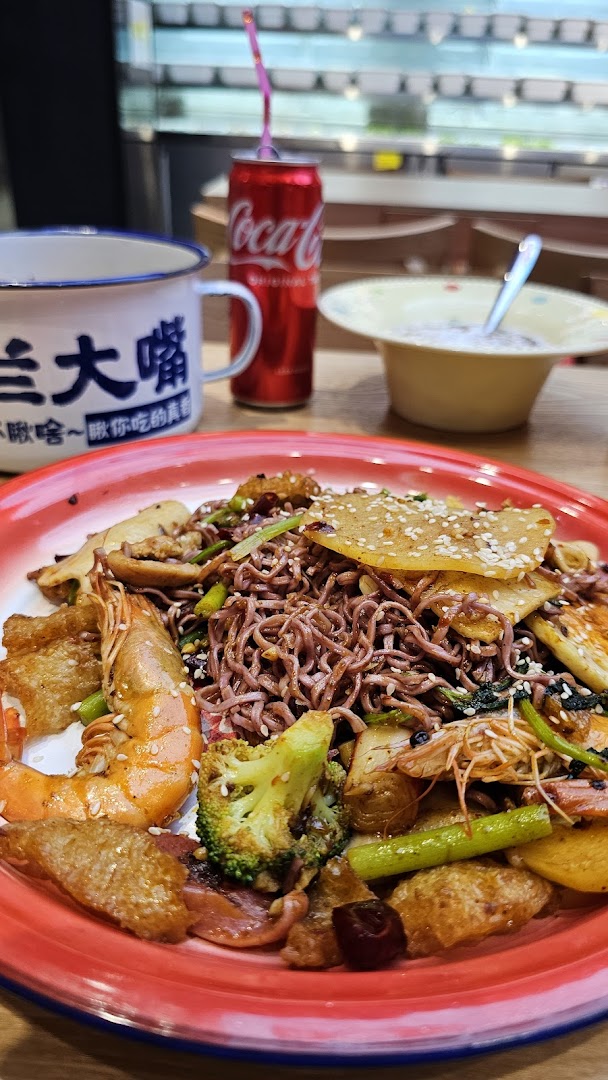 A vibrant plate of stir-fried noodles with shrimp, vegetables, and other ingredients, alongside a drink.