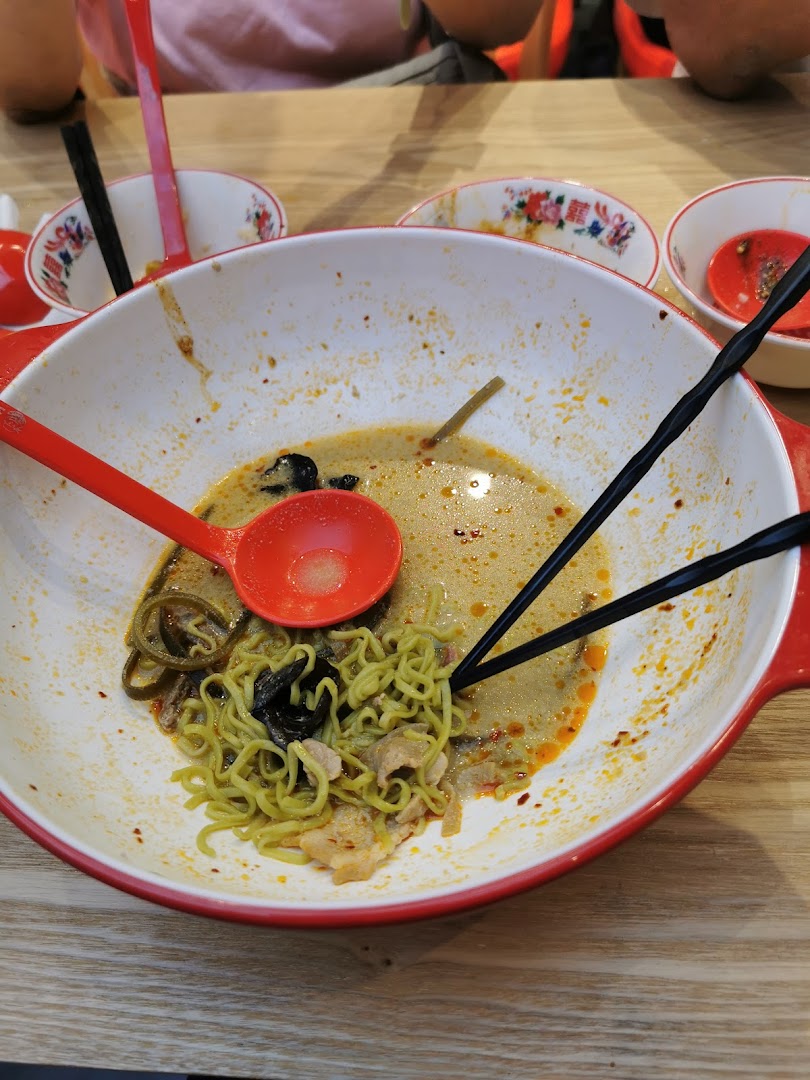 A large bowl of partially eaten green noodles with broth, chopsticks, and a spoon.