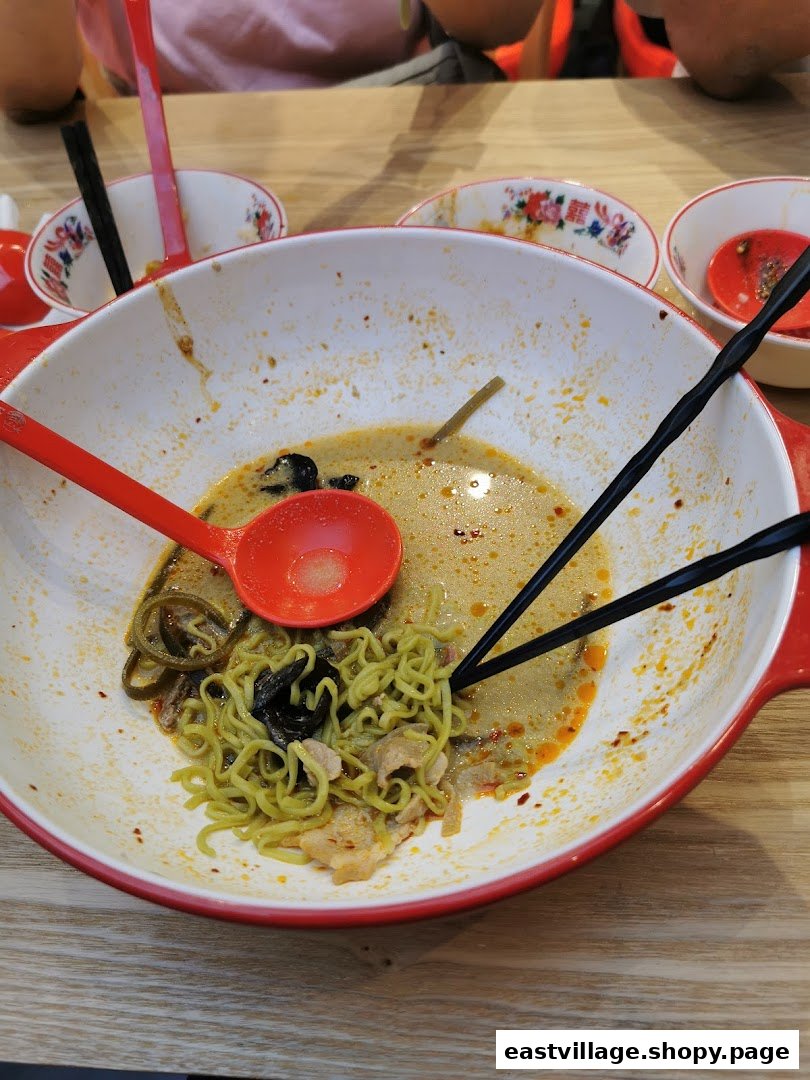 A large bowl of partially eaten green noodles with broth, chopsticks, and a spoon.