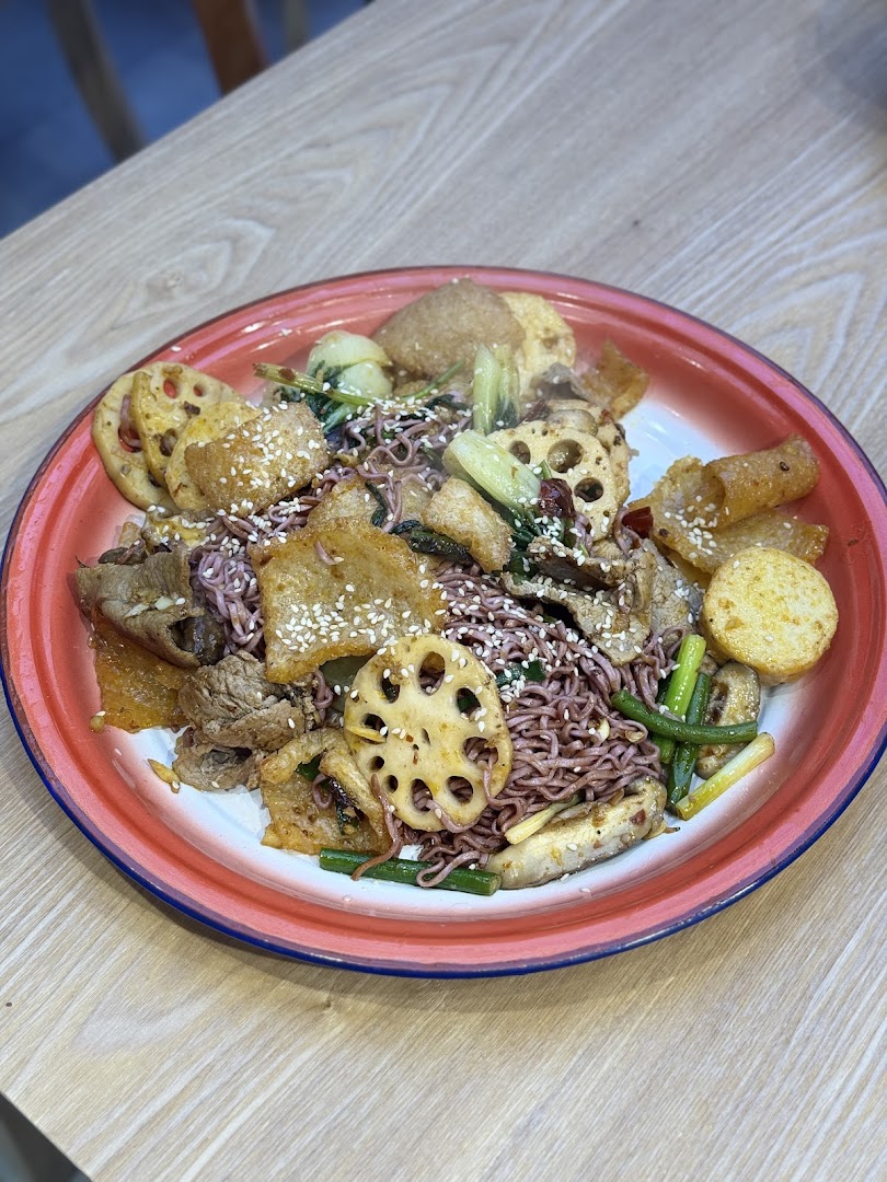A vibrant plate of stir-fried noodles with lotus root, meat, and vegetables, topped with sesame seeds.