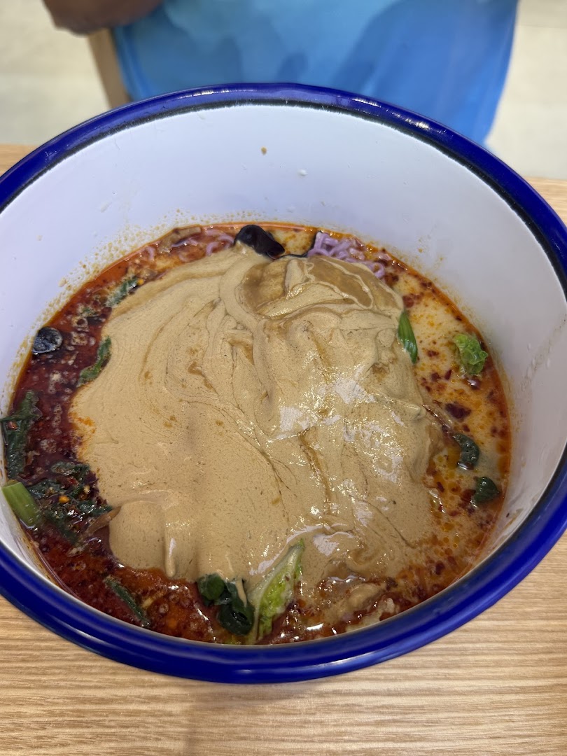 A close-up of a bowl of spicy noodles or soup with a thick, creamy topping.
