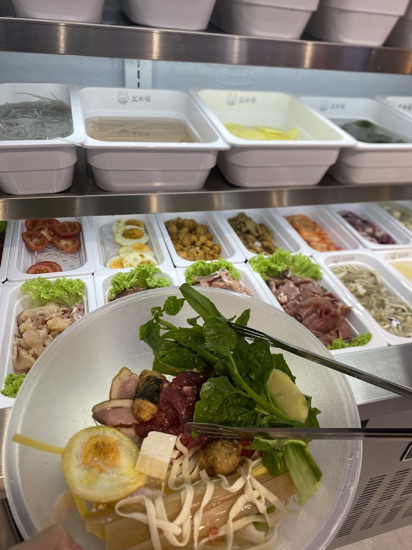 A customer's bowl filled with ingredients, with a self-service display of fresh hot pot items in the background.