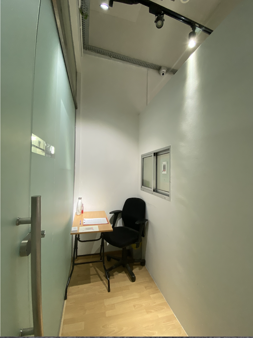 A small, minimalist room with a desk, chair, and frosted glass door, likely a waiting or consultation area.