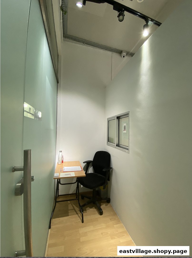 A small, minimalist room with a desk, chair, and frosted glass door, likely a waiting or consultation area.