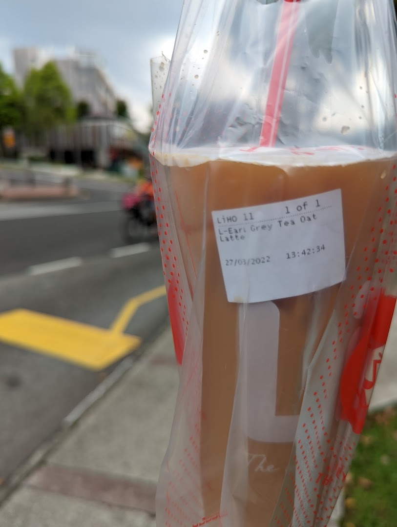 A LiHO TEA Earl Grey Tea Oat Latte in a plastic bag, held outdoors with a street in the background.
