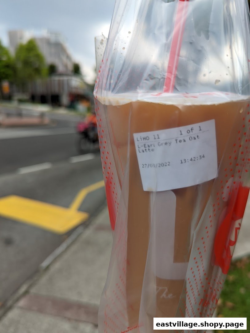 A LiHO TEA Earl Grey Tea Oat Latte in a plastic bag, held outdoors with a street in the background.