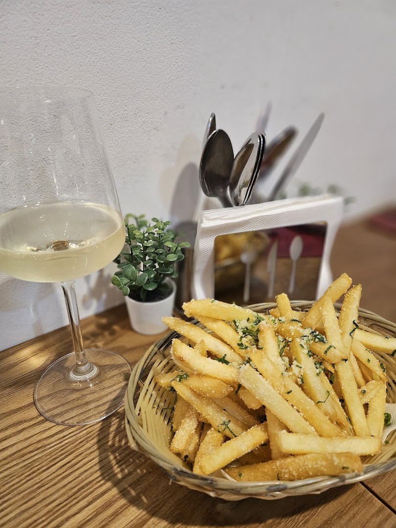 A basket of seasoned french fries and a glass of white wine on a wooden table.