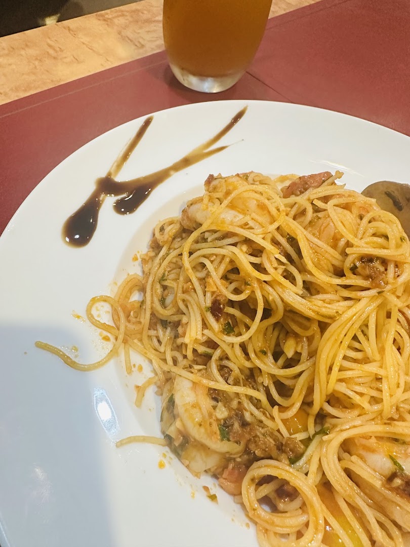 A close-up of a delicious shrimp spaghetti dish served on a white plate with a drink.