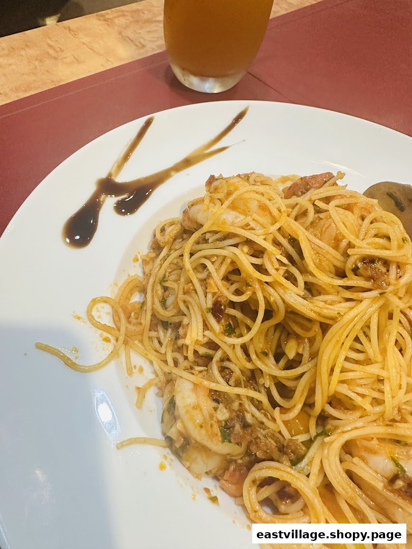 A close-up of a delicious shrimp spaghetti dish served on a white plate with a drink.