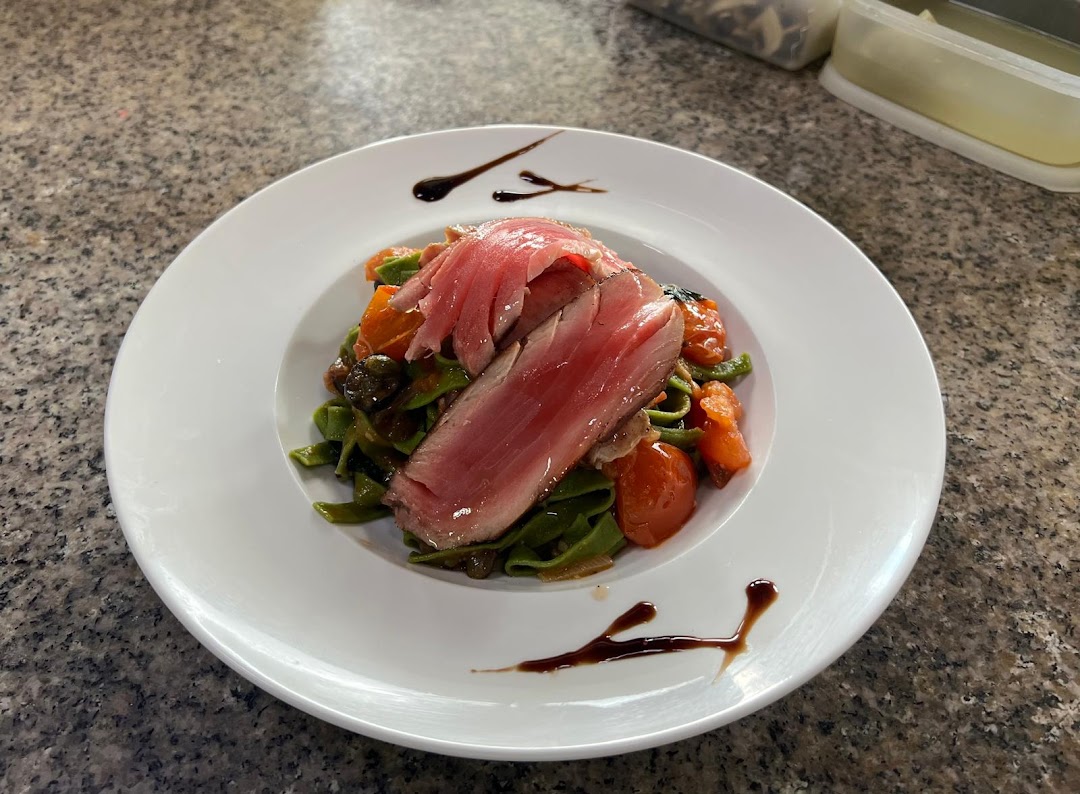 A beautifully plated dish featuring seared tuna over green pasta with cherry tomatoes and a balsamic glaze.