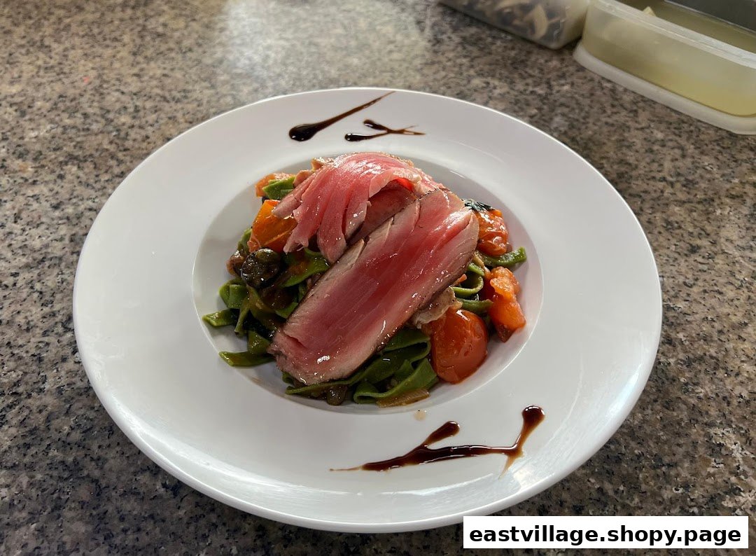 A beautifully plated dish featuring seared tuna over green pasta with cherry tomatoes and a balsamic glaze.