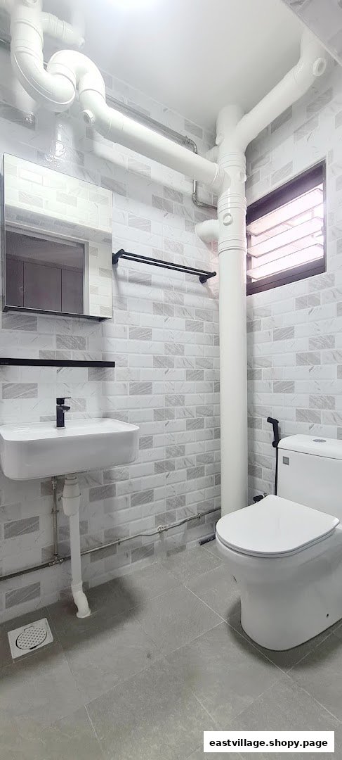 A modern bathroom featuring a white sink, toilet, and light-colored tiled walls.