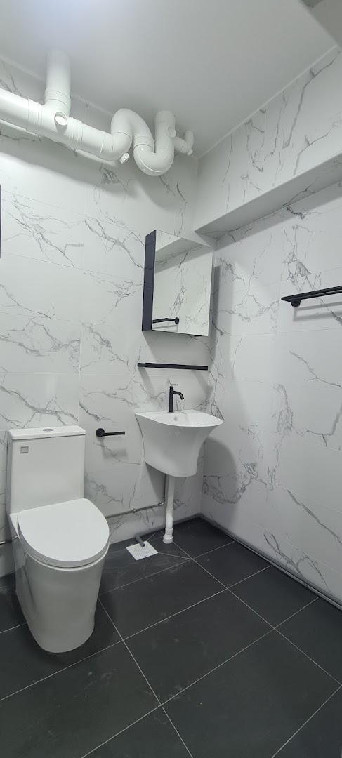 A modern bathroom featuring white marble-patterned tiles, a toilet, and a sleek sink with black fixtures.