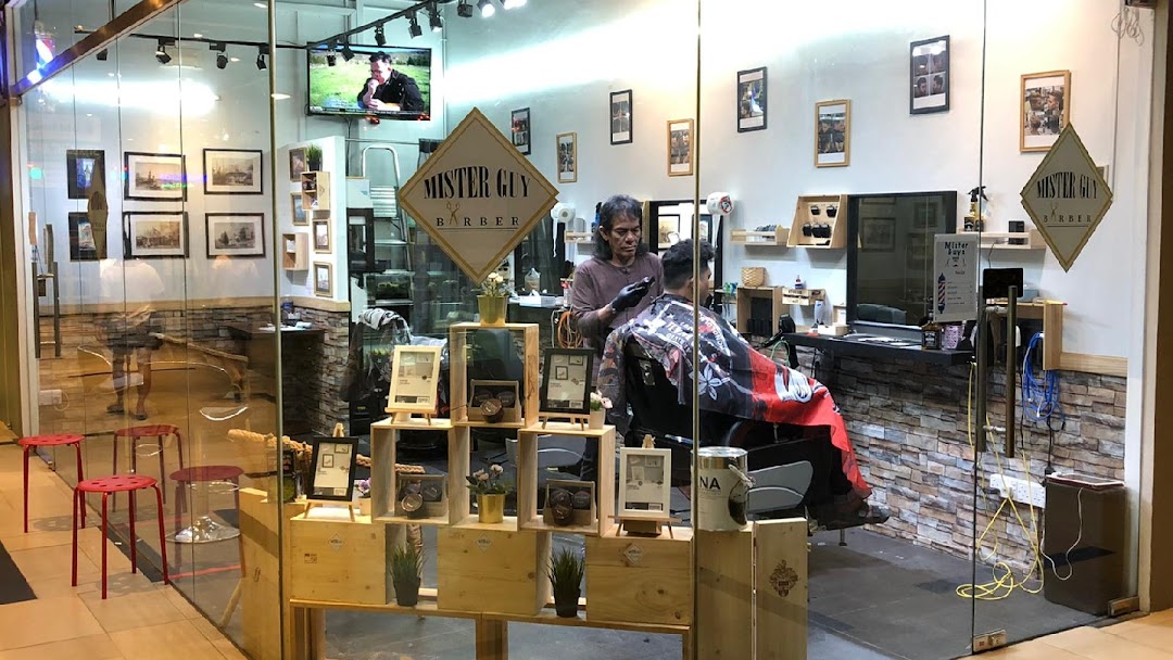 A barber is cutting a client's hair inside the Mister Guy Barber shop, visible through a glass storefront.