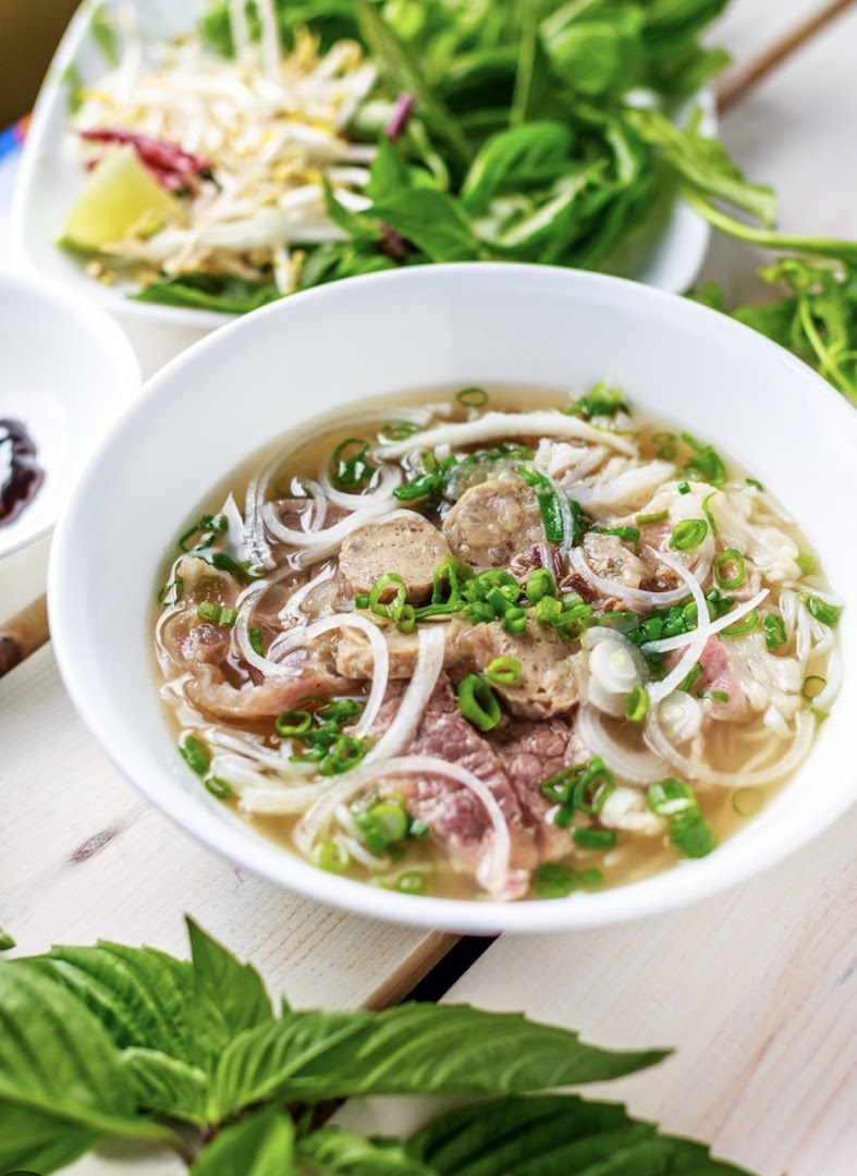 A vibrant bowl of Vietnamese pho with various meats, noodles, and fresh herbs.