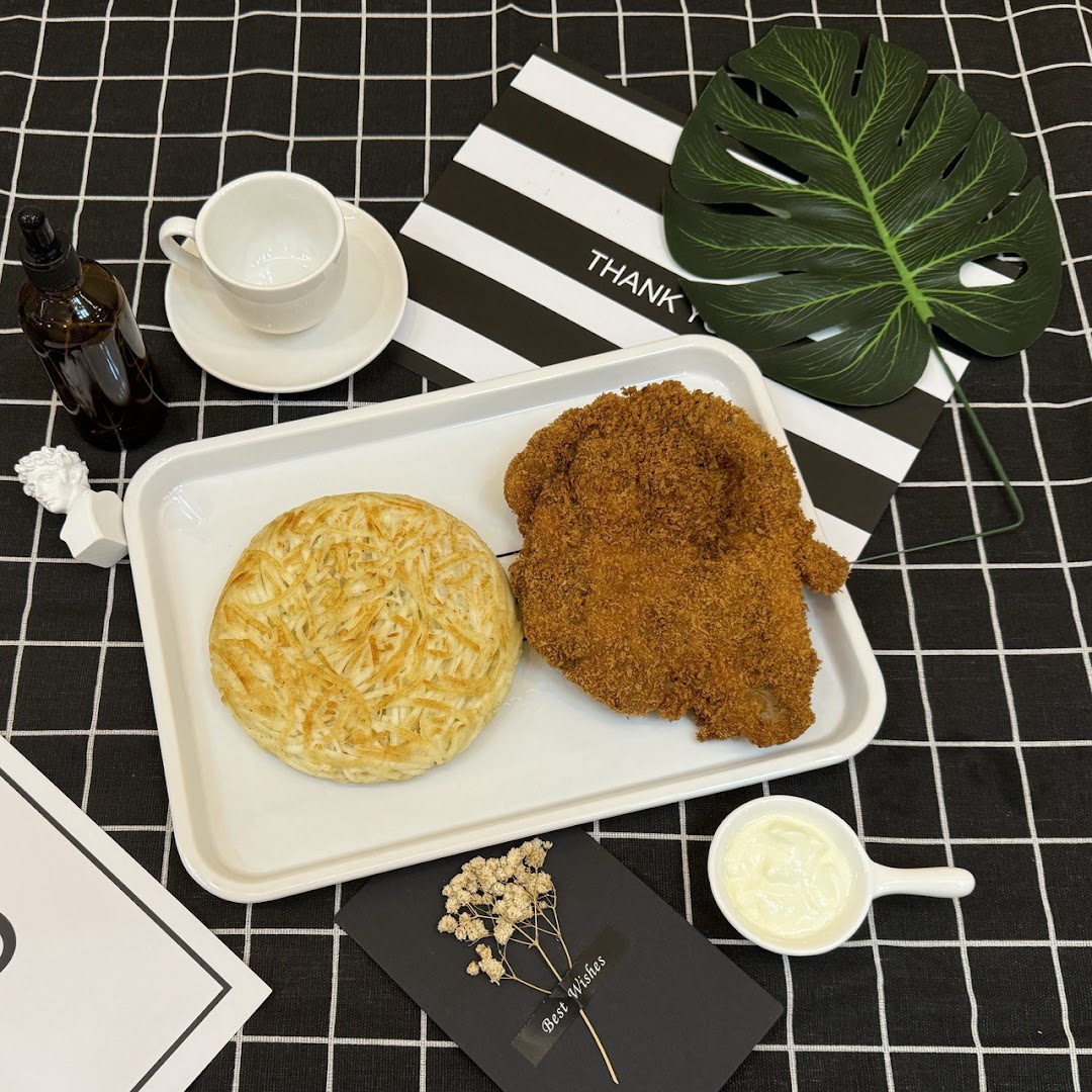 A crispy breaded cutlet and a savory potato pancake served on a tray with sauce and a cup.