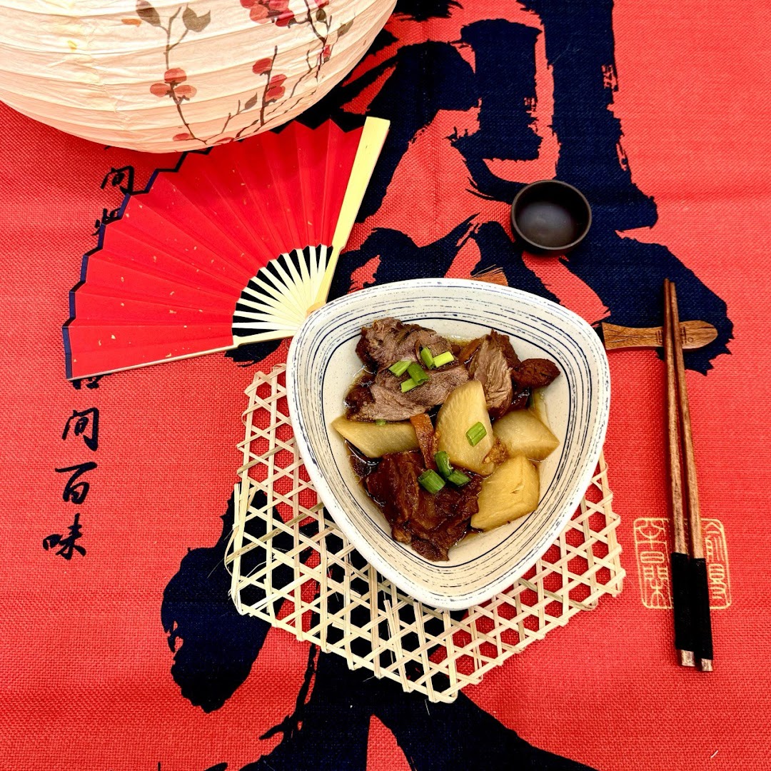 A bowl of braised meat and daikon radish with spring onions, set on a vibrant red tablecloth with traditional decor.