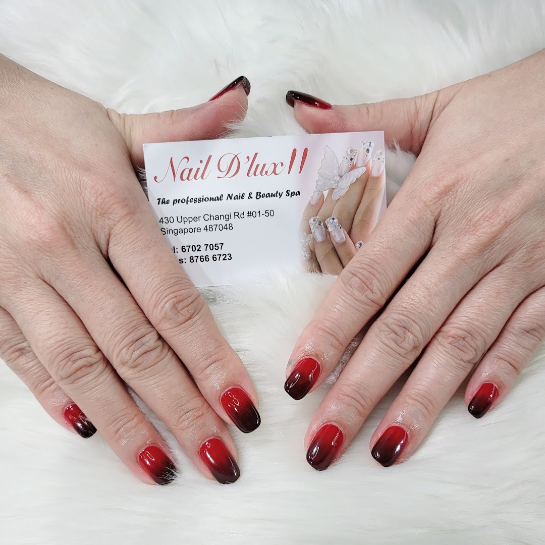 Hands with red and black ombre nails holding a Nail D'lux II business card on a white furry surface.