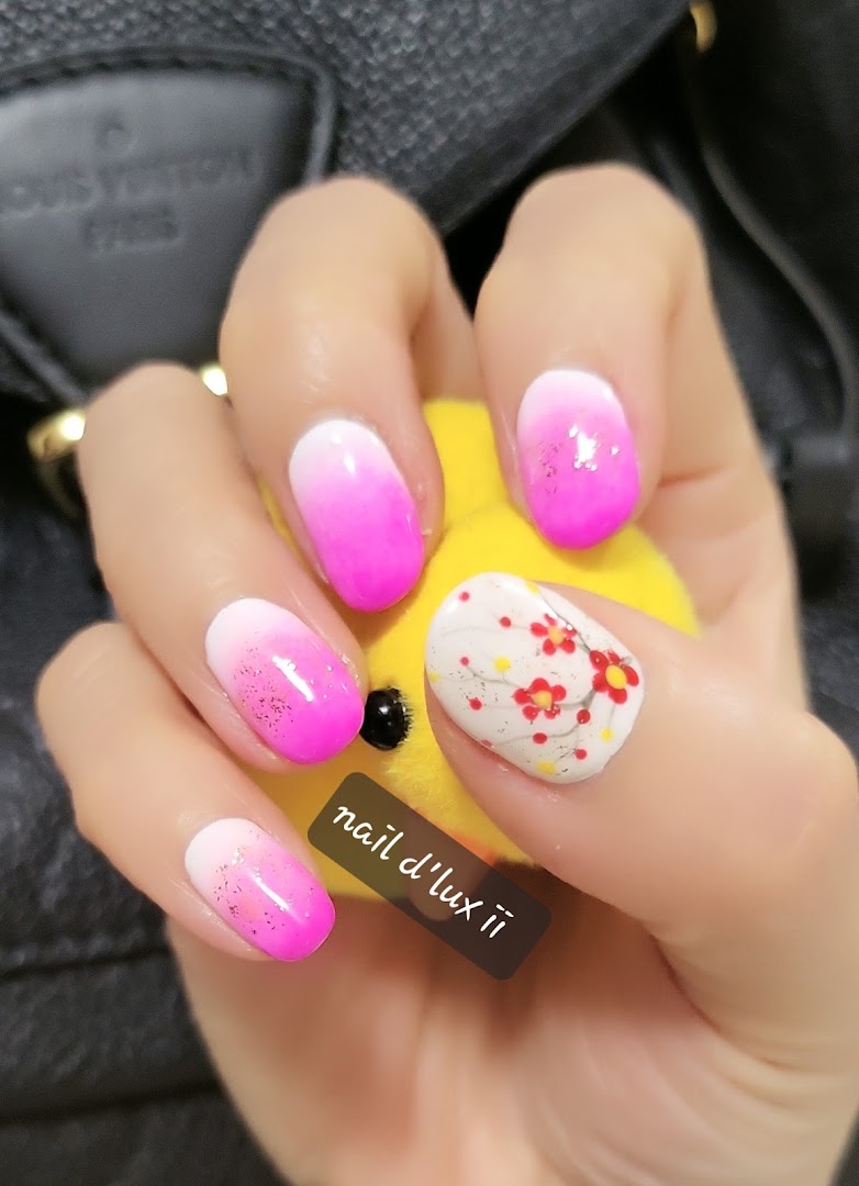 A hand showcases vibrant pink ombre nails with glitter, one featuring delicate floral art.